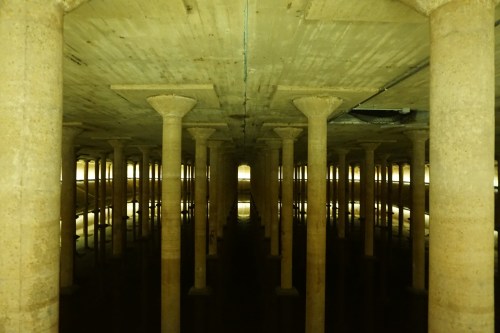 A dimly lit underground space with tall columns reflecting in still water.