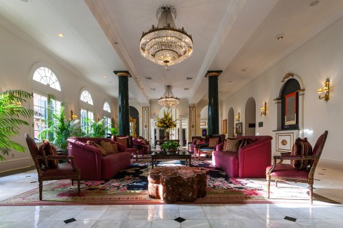 Luxurious hotel lobby with elegant seating, a chandelier, and decorative plants, featuring marble floors and rich colors.