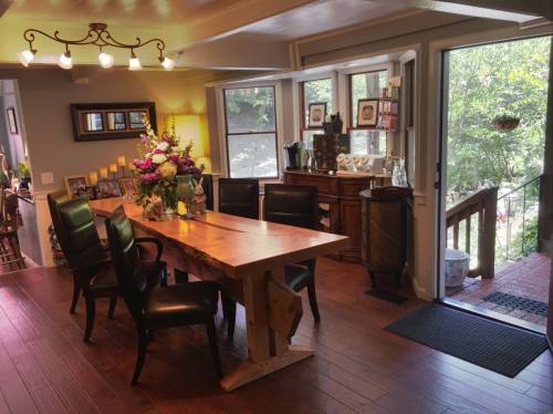 A cozy dining area with a wooden table, black chairs, and large windows overlooking greenery.