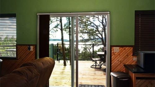 Interior view of a room with green walls, leading to a deck with a scenic view of trees and water through sliding glass doors.