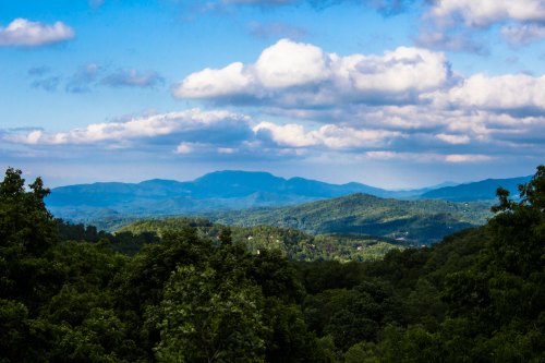 A scenic view of rolling green mountains under a blue sky with fluffy clouds.