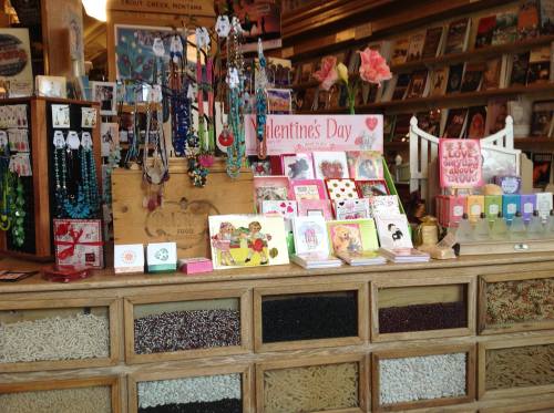 A colorful display of jewelry, Valentine's Day cards, and gifts in a charming shop with wooden shelves and decorations.