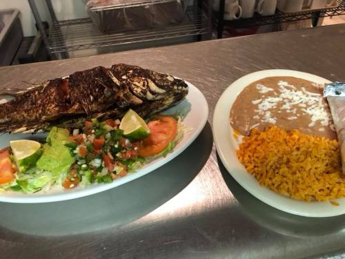 A plate with a whole grilled fish, salad, and lime, alongside rice, beans, and a tortilla.