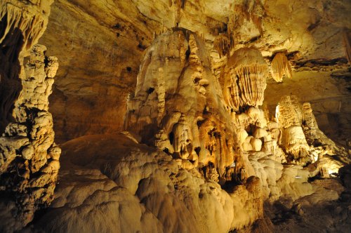 A stunning cave interior featuring large stalagmites and stalactites illuminated by soft lighting.