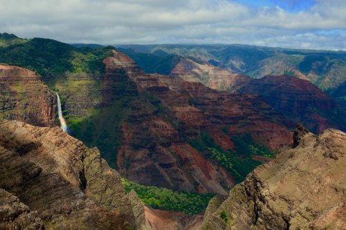 A stunning view of a canyon with layered red and green cliffs, featuring a waterfall cascading down the rocks.