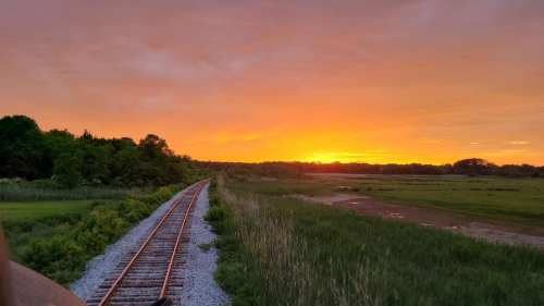 A scenic view of a railway track curving through lush greenery under a vibrant sunset sky.