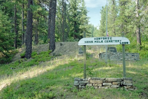 Sign for Historic Nine Mile Cemetery, surrounded by trees and greenery, with a stone wall in the foreground.