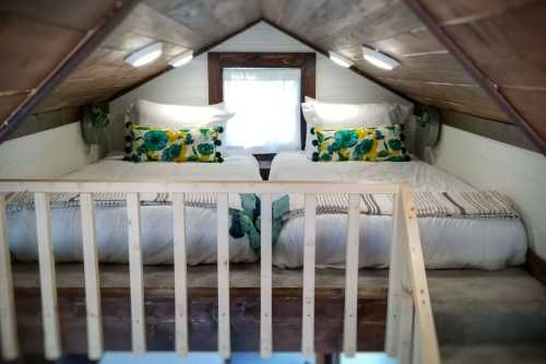 Cozy loft bedroom with two beds, floral pillows, and wooden accents under a sloped ceiling.