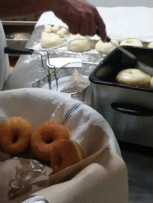 A hand prepares doughnuts, with fried doughnuts in a basket and uncooked dough in the background on a kitchen counter.