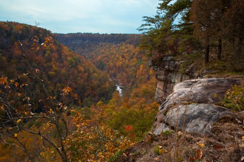 A scenic view of a valley with autumn foliage, rocky cliffs, and a winding river below.