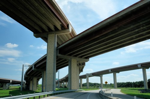 A view of multiple overpasses and highways under a blue sky with scattered clouds.