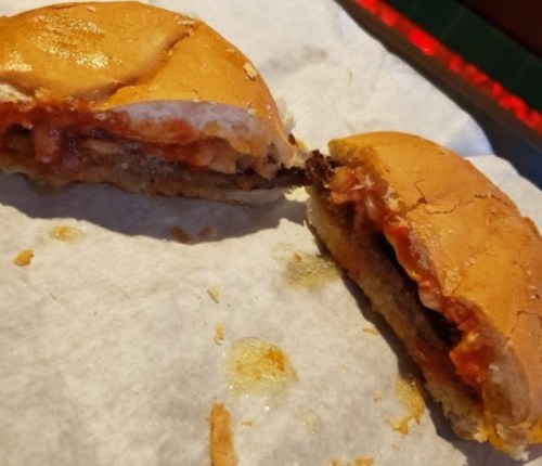 A partially eaten burger on a piece of parchment paper, revealing layers of meat, sauce, and bread.