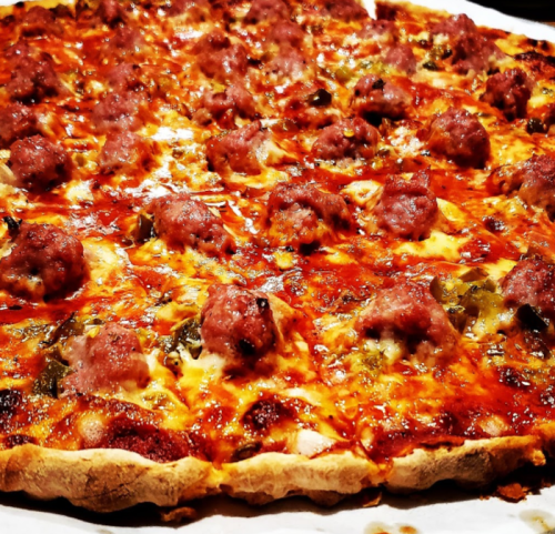 A close-up of a freshly baked pizza topped with melted cheese, meatballs, and green peppers on a golden crust.