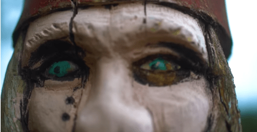 Close-up of a carved wooden figure's face, featuring striking green eyes and intricate details.