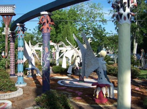 Colorful sculptures and artistic columns in a vibrant garden setting, surrounded by greenery and pathways.
