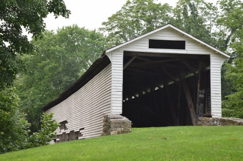 A white covered bridge with a wooden structure, surrounded by green trees and grass.