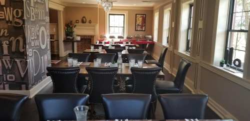 A dining room with several tables set for a meal, featuring black chairs and a decorative wall.