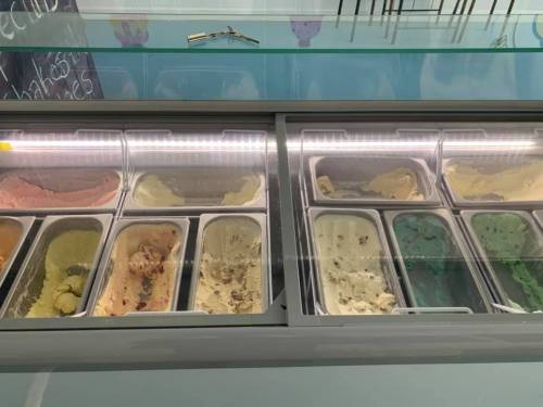 A display of various ice cream flavors in metal tubs, with colorful options including pink, green, and beige.