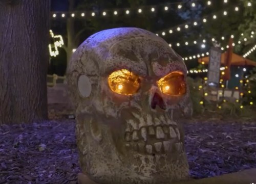 A decorative skull with glowing orange eyes, surrounded by outdoor lights and a festive atmosphere.