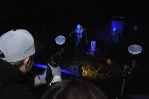 A person aims a paintball gun at a spooky figure in a dark, eerie setting with blue lighting.