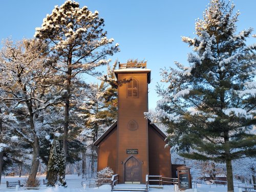 A wooden church surrounded by snow-covered trees under a clear blue sky.