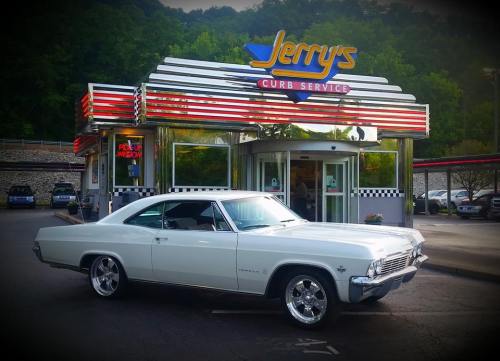 A classic white car parked in front of Jerry's Curb Service, a retro-style diner with neon signage.