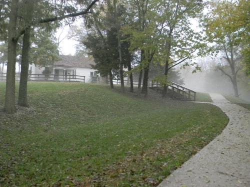 A foggy scene with a path winding through greenery, leading to a white house surrounded by trees.