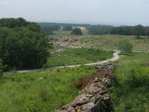 A scenic view of a winding road through a grassy landscape with rocky outcrops and trees in the background.