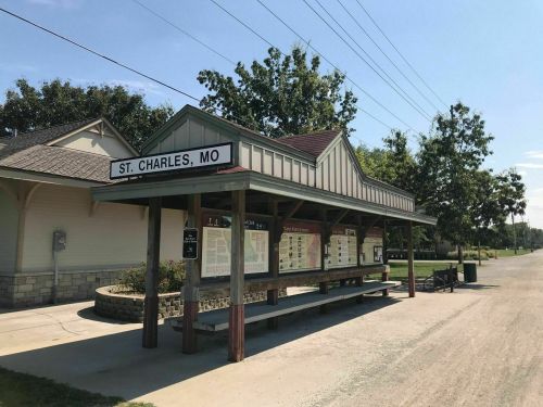 A bus stop shelter in St. Charles, MO, with informational signs and benches, surrounded by greenery on a sunny day.