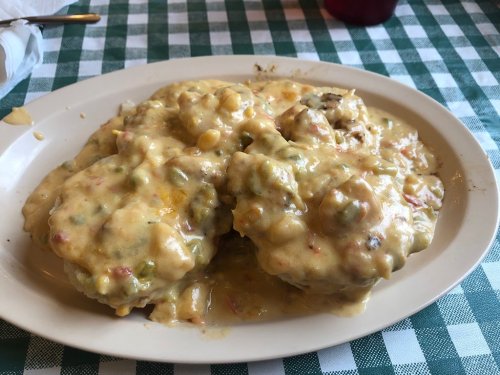 A plate of creamy, cheesy biscuits smothered in a colorful vegetable sauce, served on a checkered tablecloth.