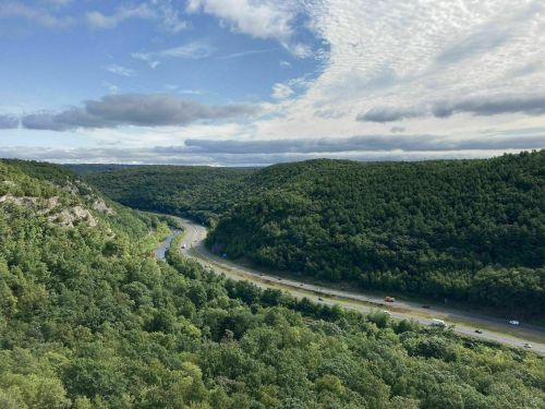 A scenic view of a winding highway through lush green hills under a partly cloudy sky.