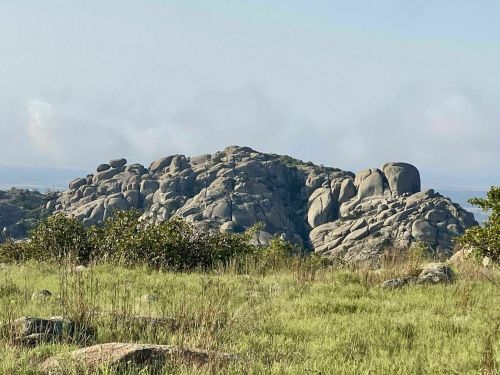 A rocky hilltop surrounded by green grass under a clear sky.