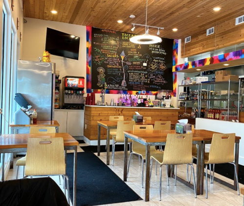 Interior of a cozy restaurant featuring wooden tables, colorful decor, and a chalkboard menu on the wall.