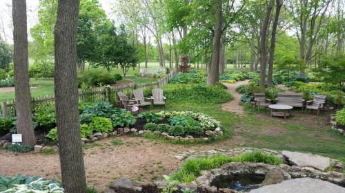A serene garden with lush greenery, stone paths, and seating areas surrounded by trees and plants.