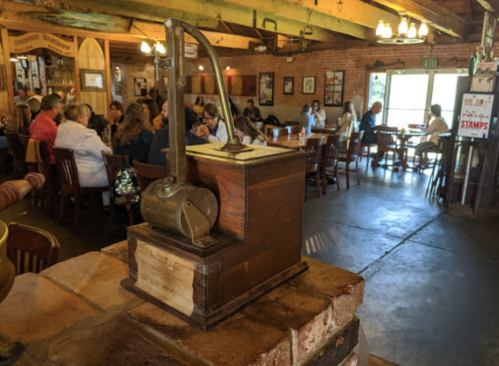 A vintage wooden device sits on a brick ledge, with a bustling restaurant scene in the background.