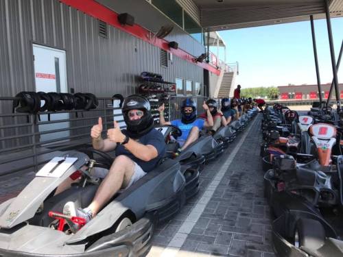 A line of go-karts with drivers in helmets, ready to race at a karting track.