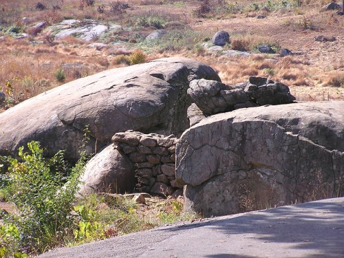 Large boulders in a dry, grassy landscape, with a small stone structure partially visible among the rocks.
