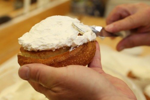 A hand spreads cream cheese frosting on a round cake or pastry with a knife.