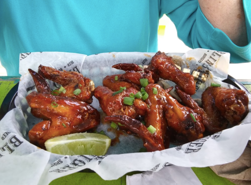 A plate of saucy chicken wings garnished with green onions and lime wedges, served on parchment paper.