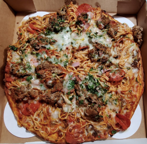 A pizza topped with spaghetti, pepperoni, ground meat, and melted cheese, served in a cardboard box.