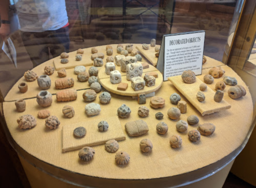A display case featuring various decorated clay objects arranged on a circular table and surrounding surfaces.