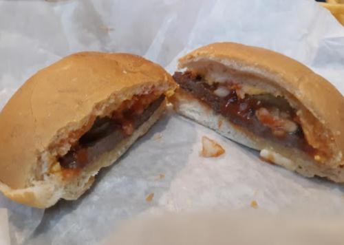 A split sandwich revealing a meat patty with sauce and toppings inside a soft bun, resting on white paper.