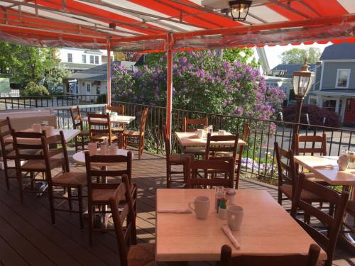 Outdoor dining area with wooden tables and chairs, surrounded by blooming flowers and a sunny street view.