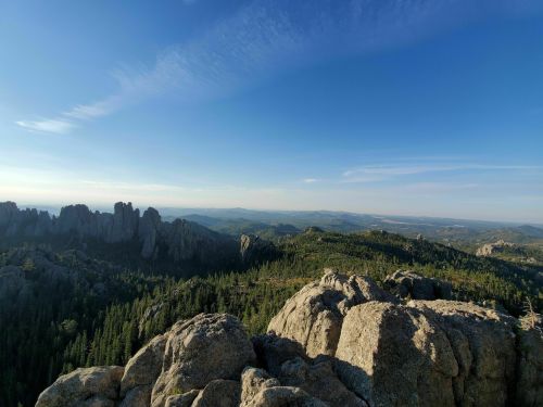 A panoramic view of rugged mountains and lush forests under a clear blue sky.