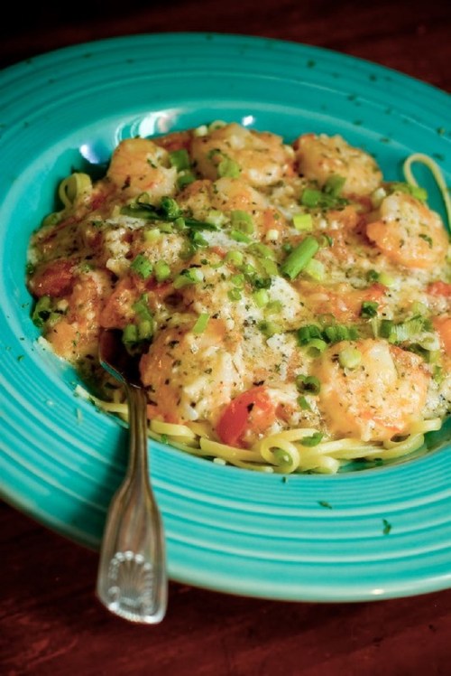A vibrant blue plate filled with shrimp pasta, topped with green onions and herbs, with a fork resting beside it.