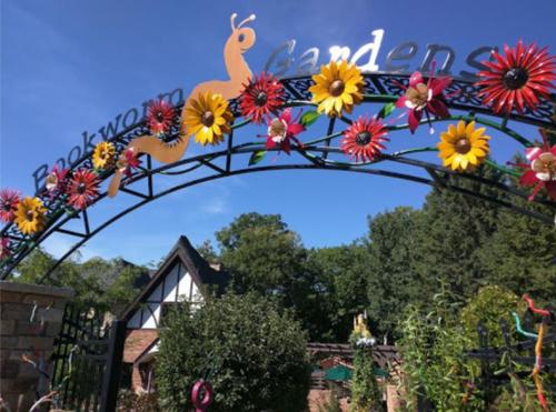 Colorful archway with flowers and a snail, welcoming visitors to Bookworm Gardens under a clear blue sky.