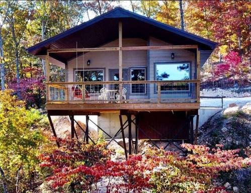 A modern cabin on stilts surrounded by colorful autumn foliage and trees.