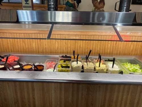 A salad bar featuring various toppings, including lettuce, tomatoes, olives, and dressings in clear containers.