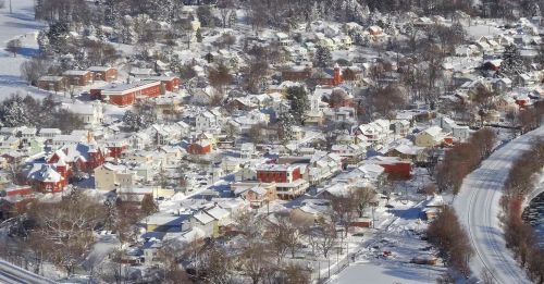 Aerial view of a snow-covered town with colorful houses and trees, alongside a winding road.