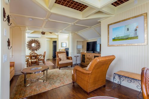 Cozy living room with wicker furniture, a coffee table, and a TV, featuring a decorative ceiling and warm color palette.